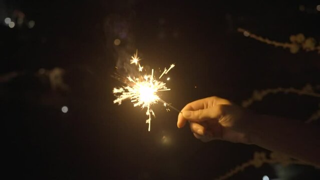This slow motion video shows a hand holding a sparkler firework stick against a night time sky.