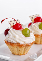 Beautiful cream cakes with cherries and grapes on a plate on a white background