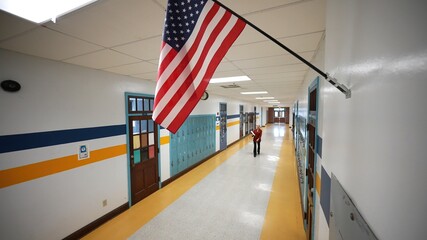 Wide angle view of front of teacher walking down empty school hallway with US American flag.