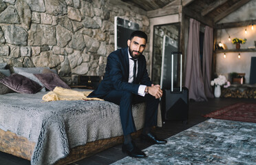 Confident young man sitting on bed in hotel room