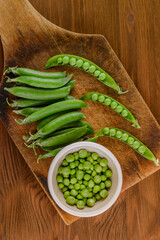 Fresh green pea and pea pods. Pea in bowl and pea pods on wooden board. Top view.