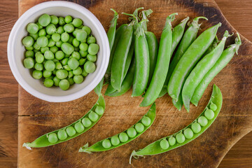 Fresh green pea and pea pods. Pea in bowl and pea pods on wooden board. Top view.