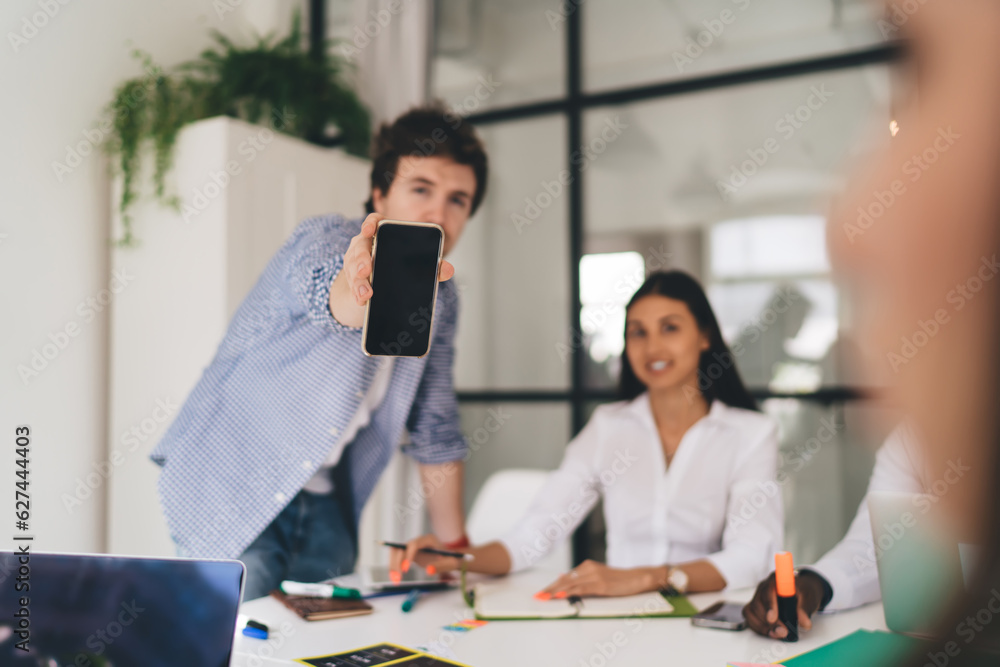 Poster man showing smartphone screen while working on project in office