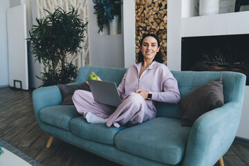 Obraz premium Smiling woman sitting with laptop on sofa