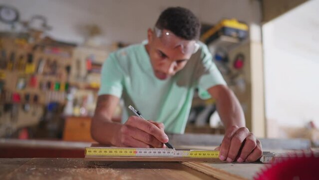 One Young black carpentry student measuring wood, preparing to use saw machine with measurement tape. Concentrated carpenter at workshop, learning profession