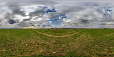 Fototapeta na wymiar spherical 360 hdri panorama among green grass farming field with clouds on overcast sky in equirectangular seamless projection, use as sky dome replacement, game development as skybox or VR content