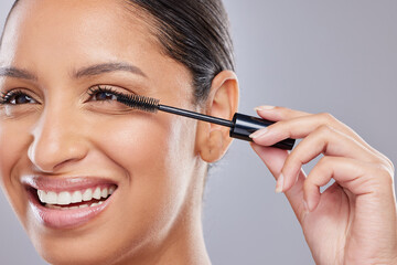 Makeup, mascara and happy woman with brush in studio for beauty, cosmetics and application on grey background. Eyelash, smile and face of Indian lady model with tool for volume, glamour or aesthetic