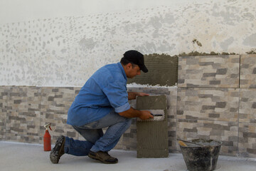 Image of a handyman tiler who with a spatula spreads the glue for laying the tiles on a house wall. Do-it-yourself work and home renovation.
