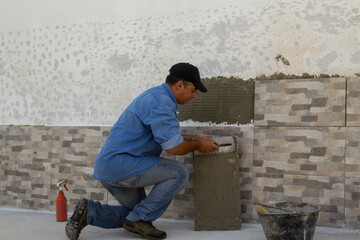 Image of a handyman tiler who with a spatula spreads the glue for laying the tiles on a house wall....