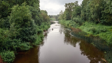 Fototapeta na wymiar Minija river in Lithuania, photographed from above from pedestrian bridge, beautiful river banks and kayakers in the distance