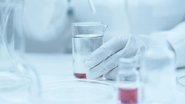 Laboratory technician mixes the red reagent with liquid in flasks. Research of medicinal properties. Chemical reactions. Mixing with water in a test tube. Red regent.
