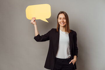 Young cheerful woman in casual over grey background showing blank yellow speech bubble.