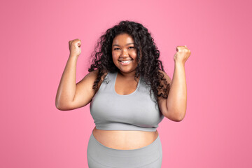 Motivation concept. Overjoyed black obese lady in sports bra and leggings cheering and raising clenched fists up