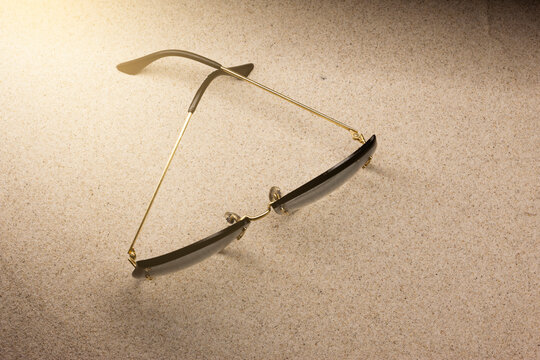 Okulary damskie plażowe, przeciwsłoneczne w złotych ramkach, leżące na piasku w ostrym słońcu. Lato i akcesoria plażowe. Ochrona przed słońcem 