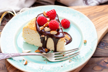 Slice of vanilla cheesecake with chocolate sauce, fresh raspberry and nuts on blue plate, close up view