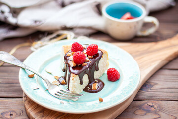 Slice of vanilla cheesecake with chocolate sauce, fresh raspberry and nuts on blue plate, close up view