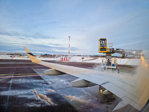 Helsinki, Finland - March 11, 2023: View from inside Finnair airplane. Service worker spraying de-icing and anti-icing fluids to  plane before take-off. Ground deicing of aircraft.