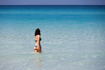 Woman in bikini walking in blue sea water. Beach vacation on Caribbean islands