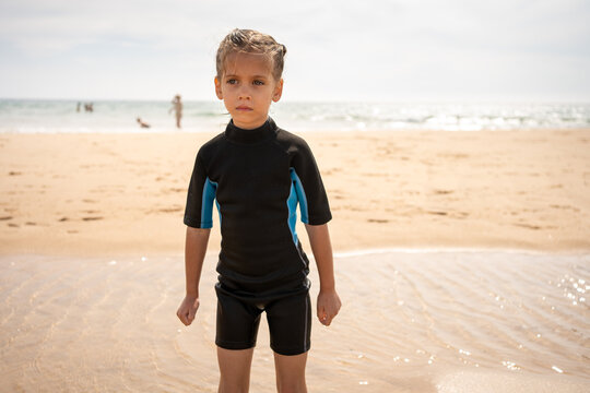 Little girl surfer in wetsuit standing ocean beach