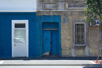Fototapeta na wymiar Facade of old house on street of Georgian city of Tbilisi. White window and wooden blue door. Summer landscape in pastel colors. Minimalistic urban photo. Copyspace. Copy space for text. Town district