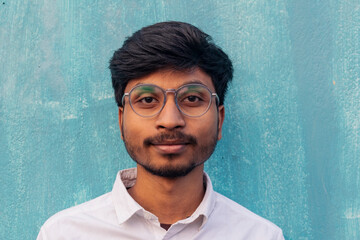 A brown boy portrait looking at the camera wearing white shirt with little beard. wearing glasses