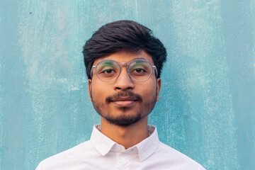 A brown boy portrait looking at the camera wearing white shirt with little beard. wearing glasses