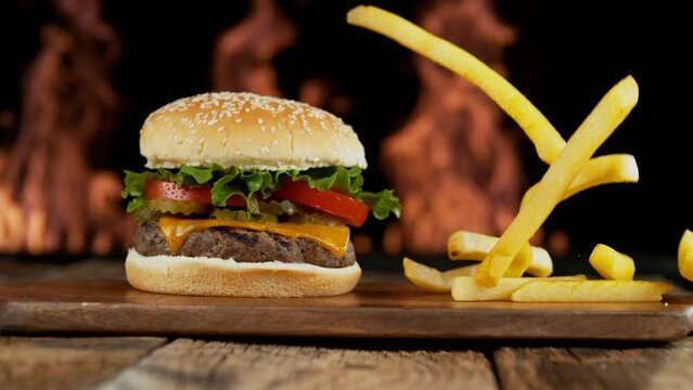 Hamburger with flames in background and french fries falling in slow motion
