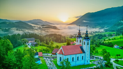 Aerial drone view of small beautiful church on valley in Slovenia at dawn. Beautiful summer morning landscape..