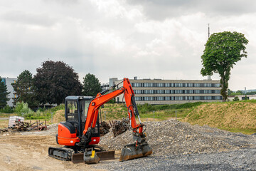 A small red excavator next to a pile of gravel at a construction site.