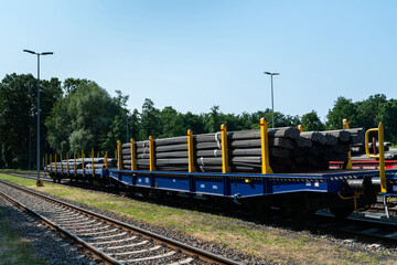 Railway platforms with bundles of black metal pipes stacked on them.