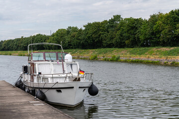 A small boat is moored to a pier on a small river.