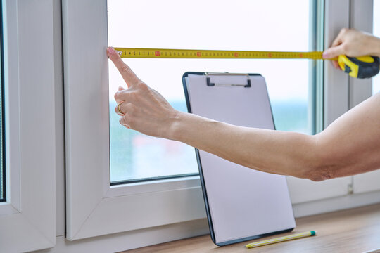 Woman measuring window with tape measure, tailoring service