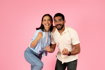 Thrilled happy young couple celebrating success on pink background