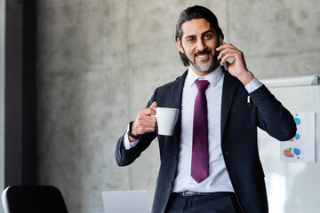 Handsome businessman drinking coffee, talking on phone at office