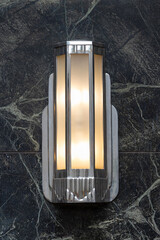 chrome and glass art deco sconce light fixture, illuminated on a dark green marble wall, close up