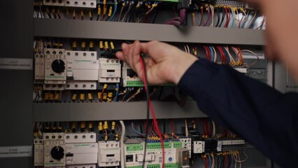 Electrical technician, Multimeter testing, Panel diagnostics. Electrician uses multimeter to check electrical current in control panel at factory.