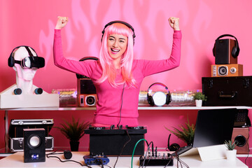 Performer with pink hair performing techno music using dj mixer console enjoying to play song with fans, having fun in club at night. Artist doing performance with professional audio equipment