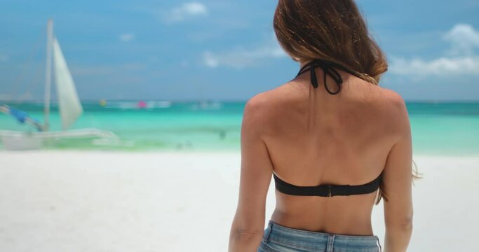 Woman in bikini walks white sand beach on tropical Boracay island, Philippines. Long hair Caucasian girl back view enjoys wild nature landscape, turquoise water and blue sky. Travel, tourism, holiday