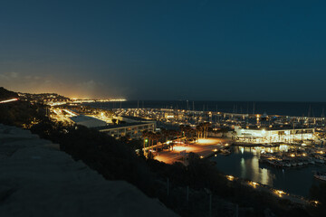 Naklejka na ściany i meble Mountain view of a maritime headland night city in Barcelona with lights and boats and restaurants