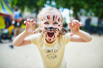 Little preschooler girl with tiger face painting outdoors
