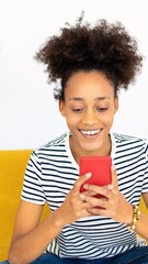 Vertical shot of young african woman using smartphone while sitting on couch at home. Technology and social media concept.