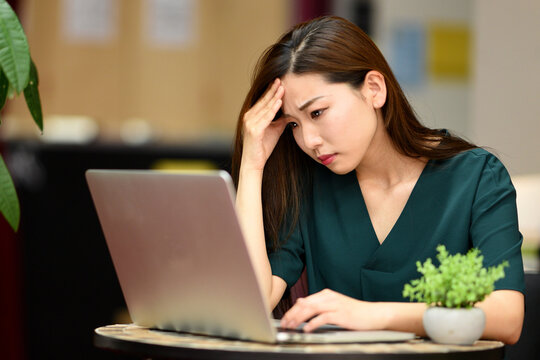 ノートパソコンの前で悩むアジア人女性

