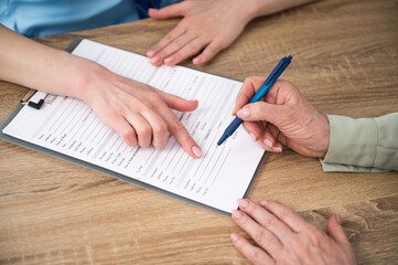 Mature patient signing insurance legal document at appointment with doctor.