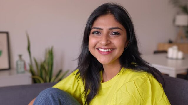 Portrait of happy young indian woman smile at camera sitting on sofa at home. Cheerful head shot of millennial female native of India relaxing on couch. Real ethnic people.