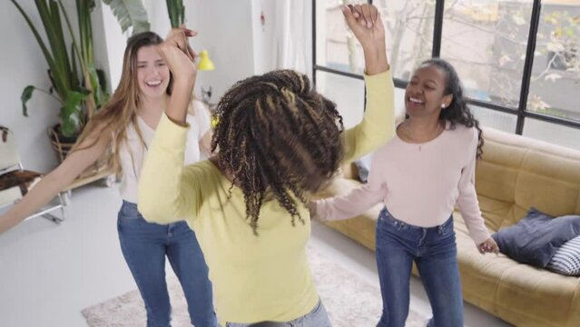 Group of young friends dancing fun at home. Cheerful trio of multiracial women enjoy music together. Happy party people. Female evening indoors. Video with afro girl in the lead role.