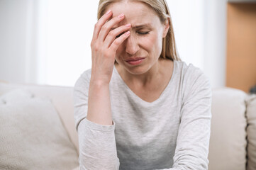 Sad tired young woman touching forehead and suffering from migraine