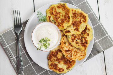 Zucchini pancakes with cream sauce on plate. Healthy diet food. Dinner table setting.