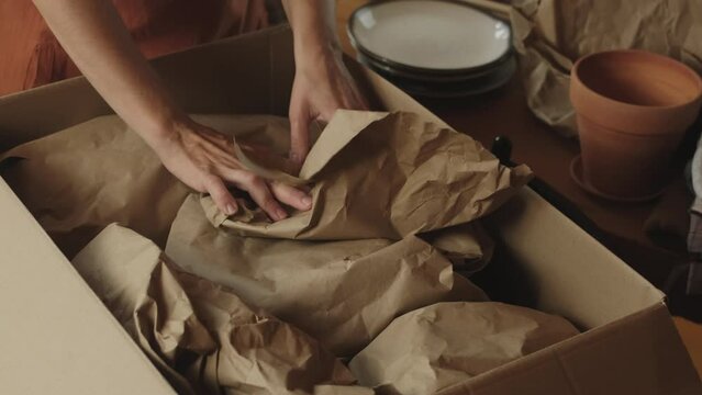 Preparing for a move. Hands packing ceramic plates into carton box.