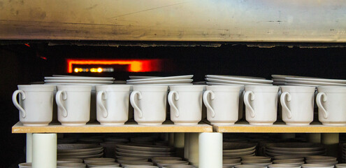 Ceramic white mugs are fired in a muffle furnace at high temperature at a porcelain factory in...