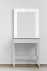 Modern white makeup dressing table with mirror and backlight on a white wall close-up.